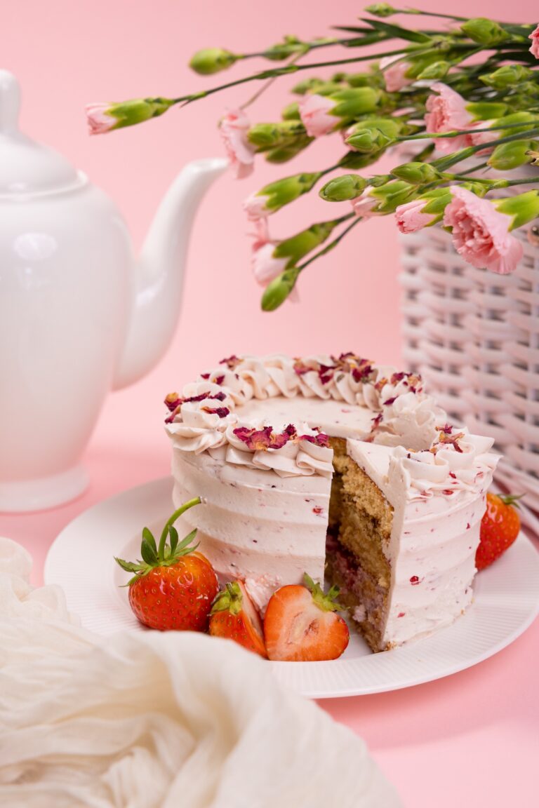 Cream cake with rose petals, strawberries, a teapot and carnations on a pink background