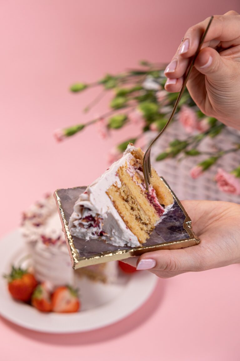 Hand holding a fork over a slice of cream cake with strawberries