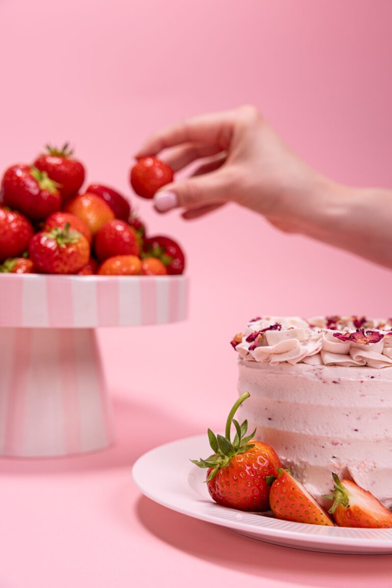 Hand reaching for a strawberry from a cake stand above a rose petal cake