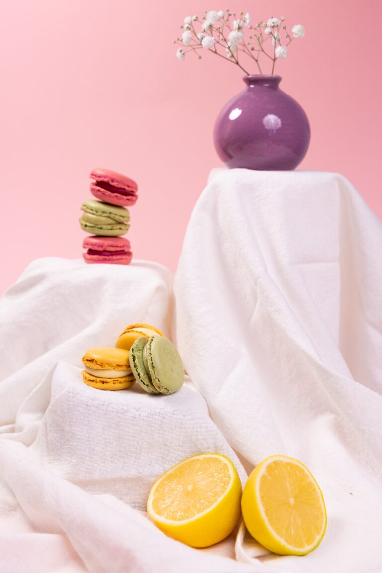 Colourful macarons on white fabric with a lemon and a purple vase of gypsophila